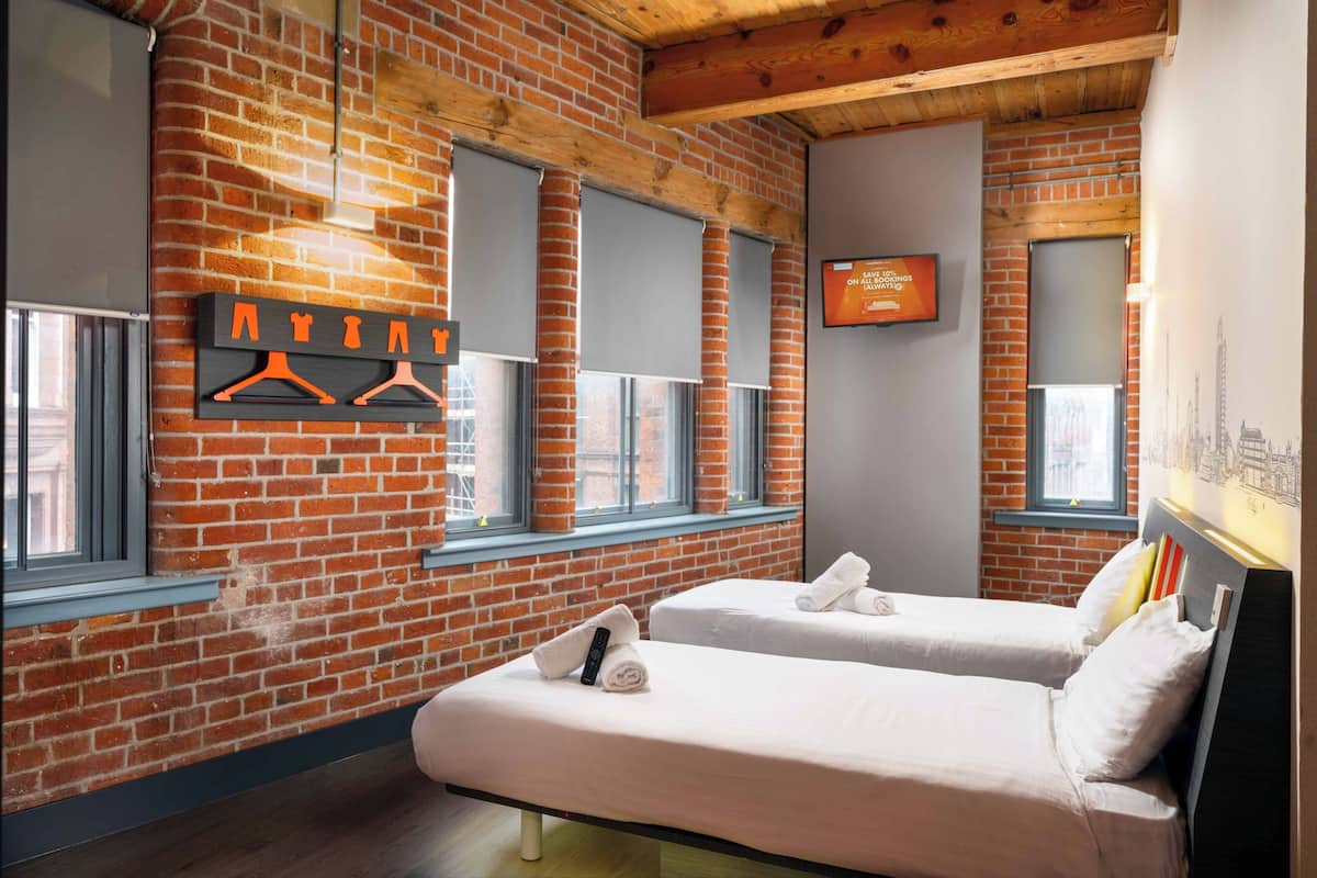 A hotel room with brick walls, wooden beams, two beds, a TV, and a wall-mounted towel rack.