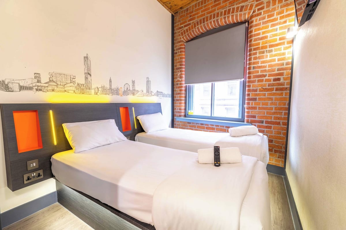 A hotel room with two beds, a cityscape mural, a brick wall, and a window.