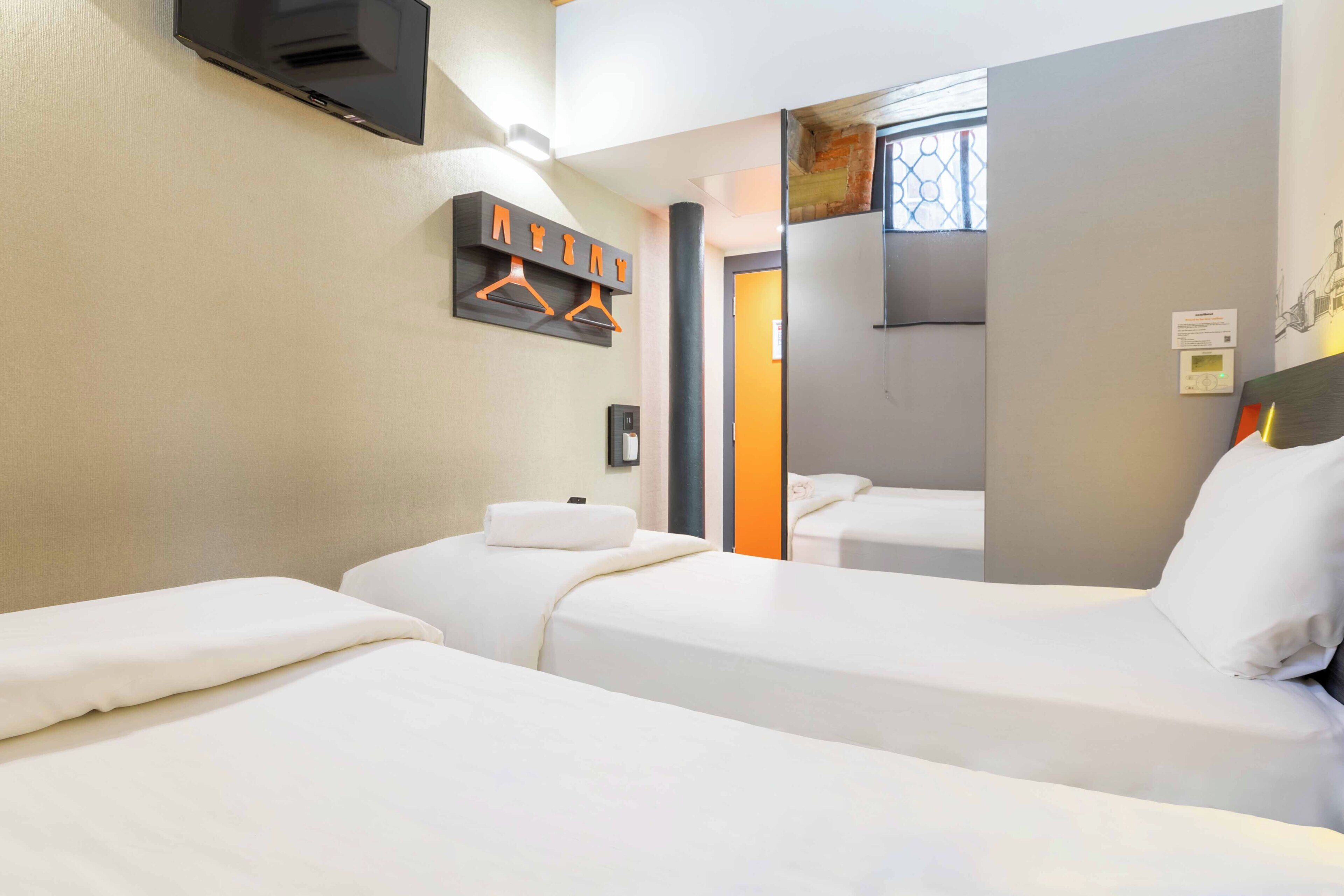 A hotel room with two beds, a TV mounted on the wall, a coat rack, and a window with a view.