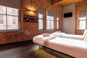 A room with two beds, a brick wall, large windows, and a hanging garment rack.