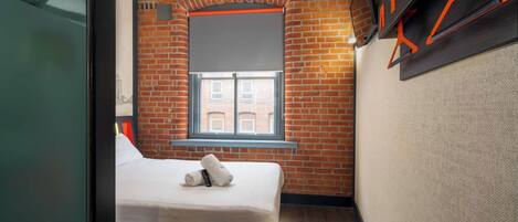 A compact room with a brick wall, a window, a bed, and a wall-mounted TV.