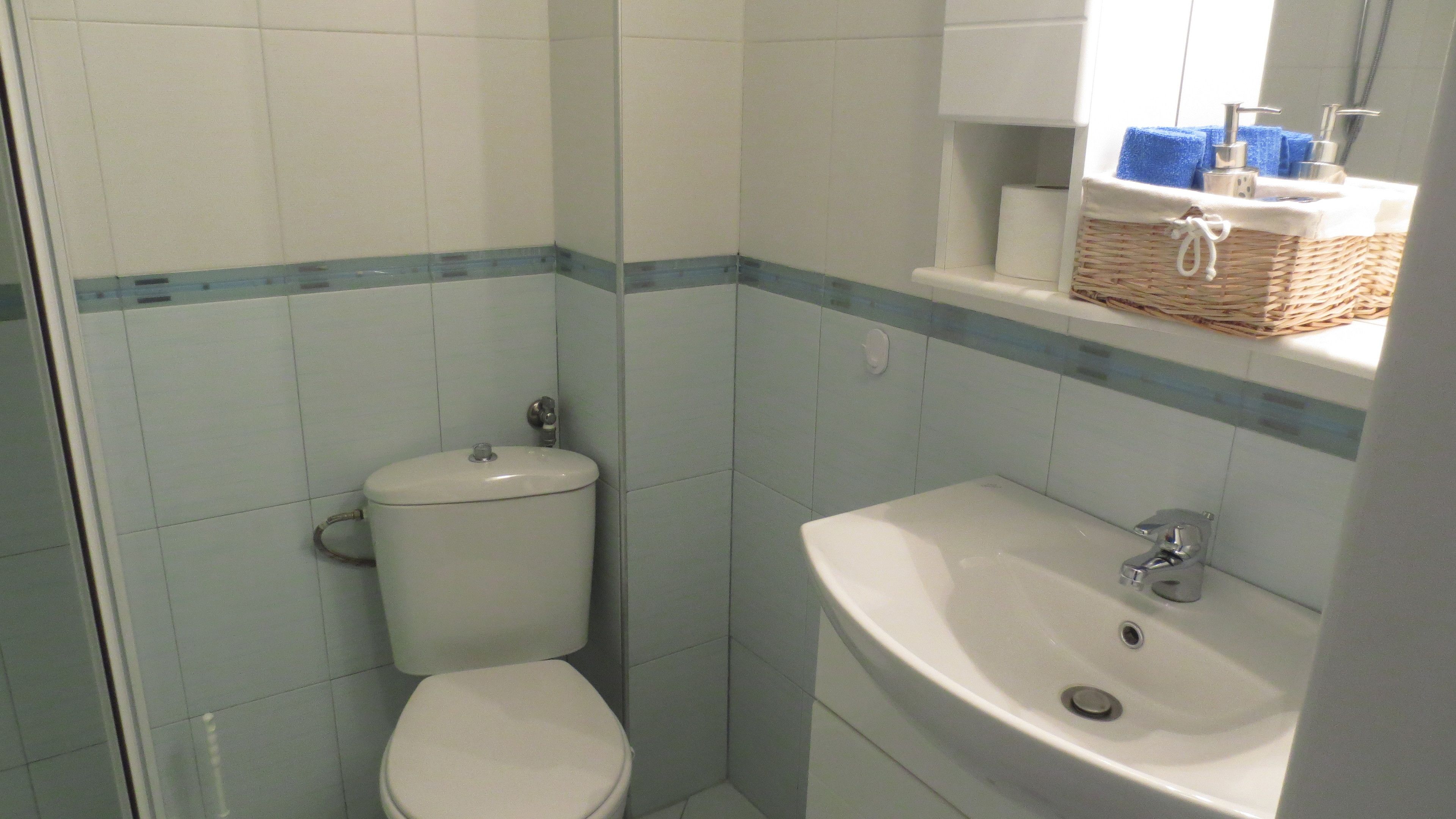 Un baño con inodoro, lavamanos y un pequeño estante con artículos de aseo.