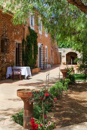 A courtyard with a table and chairs, a stone wall, and a flower pot. - Agroturísme Ca'n Gaià (Felanitx)