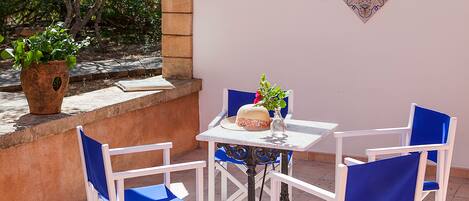 Un patio con sillas y una mesa blancos, una planta en maceta y un azulejo decorativo en la pared.