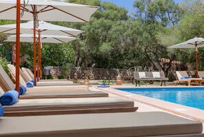 A poolside area with sun loungers and umbrellas, a stone wall, and trees in the background. - Agroturísme Ca'n Gaià (Felanitx)