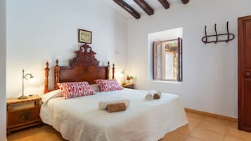 A bedroom with a wooden bed, white bedding, a nightstand with a lamp, and a window with a view.