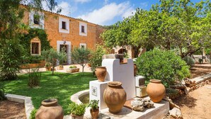 Un patio con un edificio de piedra, macetas de terracota y una pequeña fuente.