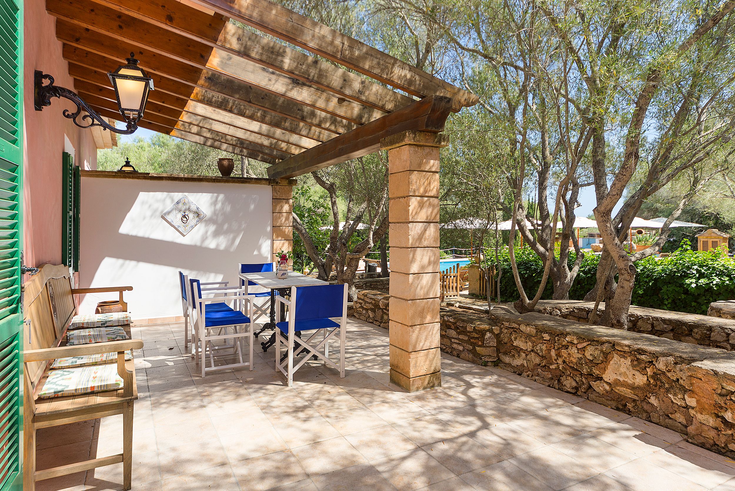 Eine Terrasse im Freien mit einer Holzpergola, einem Tisch mit blauen Stühlen und einer Steinmauer.