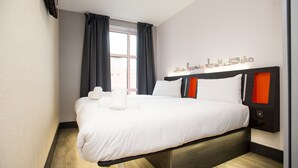 A modern hotel room with a large bed, a cityscape wall art, and a window with curtains. - easyHotel Sheffield (Sheffield)