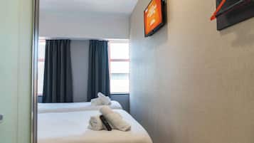 A hotel room with two beds, a TV mounted on the wall, and a window with curtains.