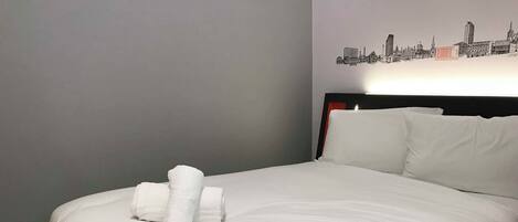 A neatly made bed with white linens and a cityscape wall art.