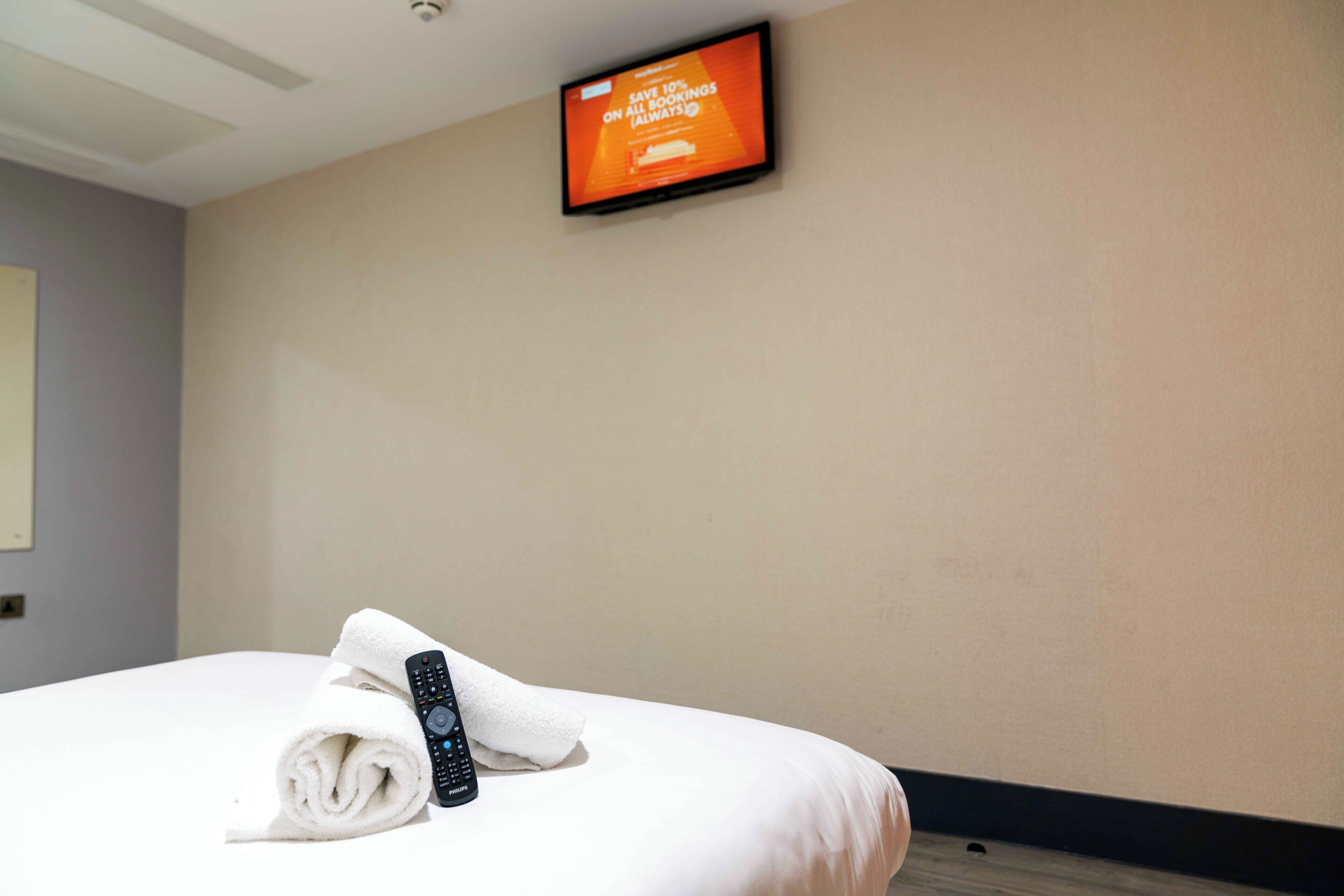 A hotel room with a bed, a remote control, and a television displaying a promotional message.