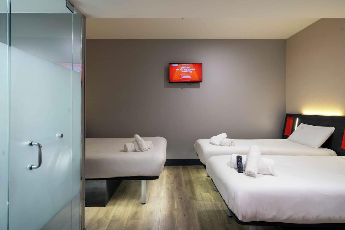 A hotel room with two beds, a TV on the wall, and a glass door.