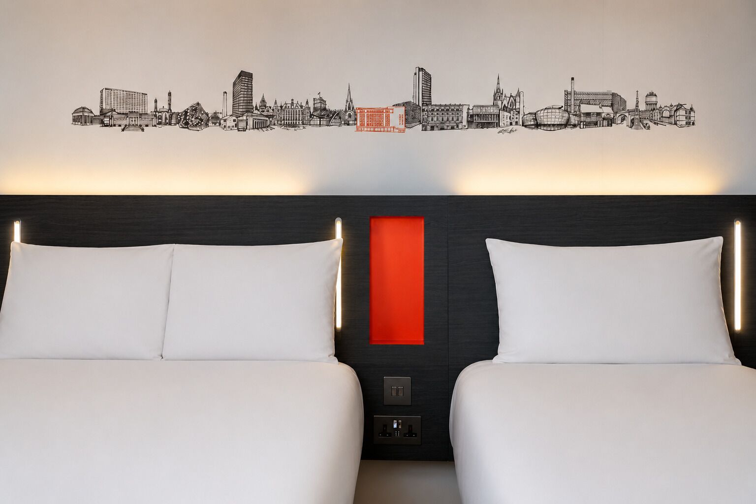 A hotel room with two beds, a cityscape wall art, and a red accent wall.
