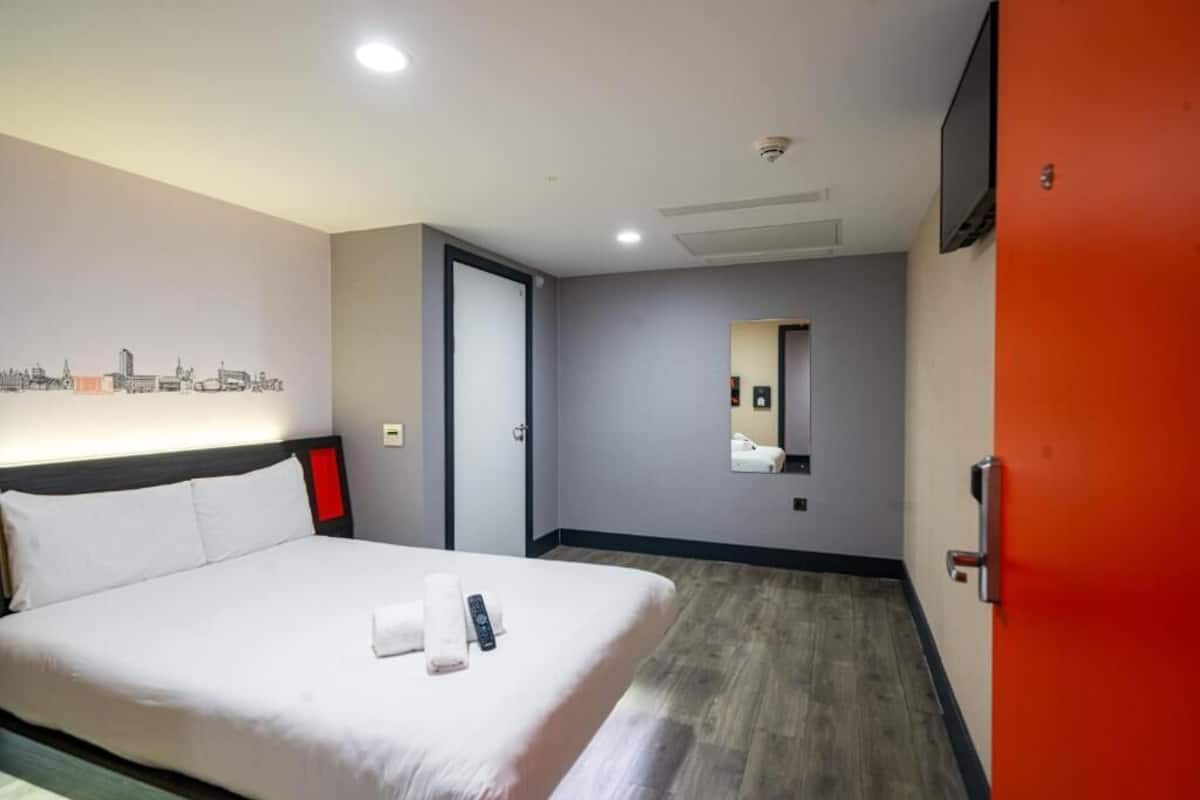 A hotel room with a bed, a wall-mounted TV, a door, and a mirror.