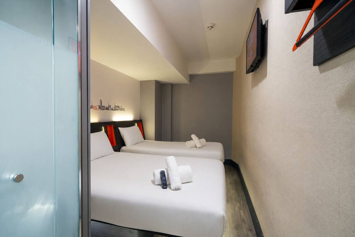 A hotel room with two beds, a flat-screen TV, and a cityscape artwork on the wall.