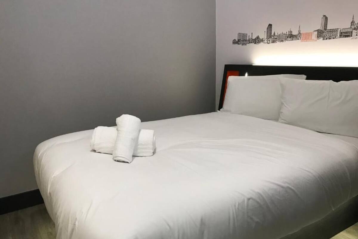 A neatly made bed with white linens and a cityscape wall art above it.