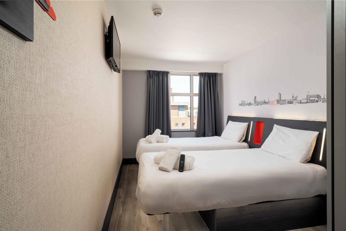 A hotel room with two beds, a cityscape view, a flat-screen TV, and a window with curtains.
