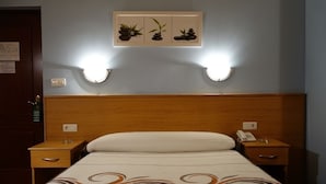A hotel room with a wooden headboard, a bed with a patterned bedspread, two bedside tables with lamps, and a wall-mounted artwork above the bed. - Hotel Reyes de León (Santa Maria del Paramo)