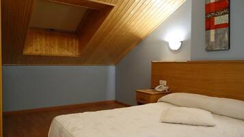 Un dormitorio con techo inclinado, cabecera de madera, mesita de noche con un teléfono y una cama con almohadas.