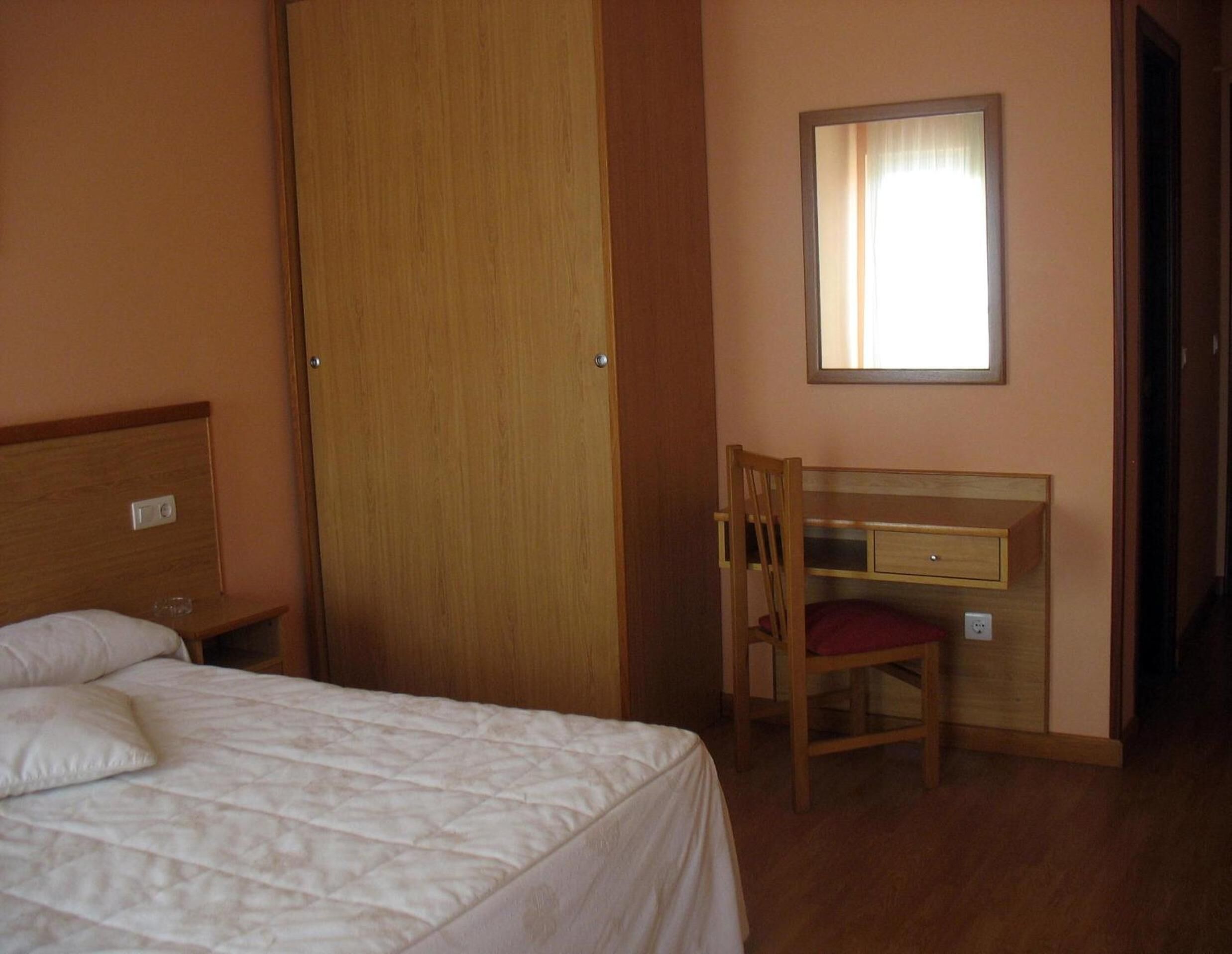 A bedroom with a bed, a wooden desk, and a chair.