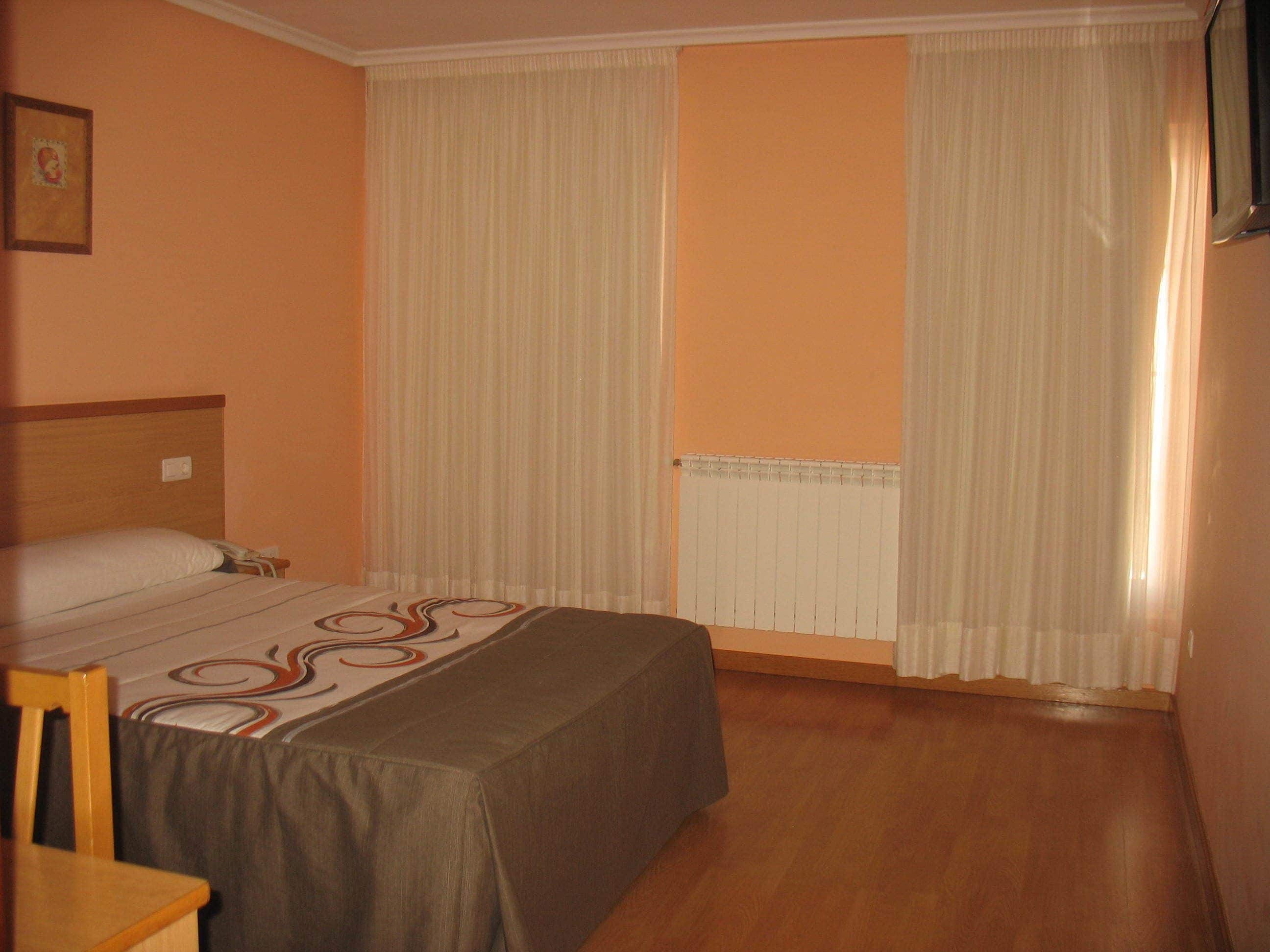 Una habitación de hotel con cama, una silla, un radiador y cortinas.