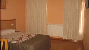 Una habitación de hotel con cama, una silla, un radiador y cortinas.