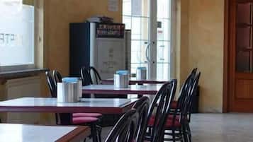 A hotel dining area with tables and chairs, a bar area with stools, and a view of the street outside.