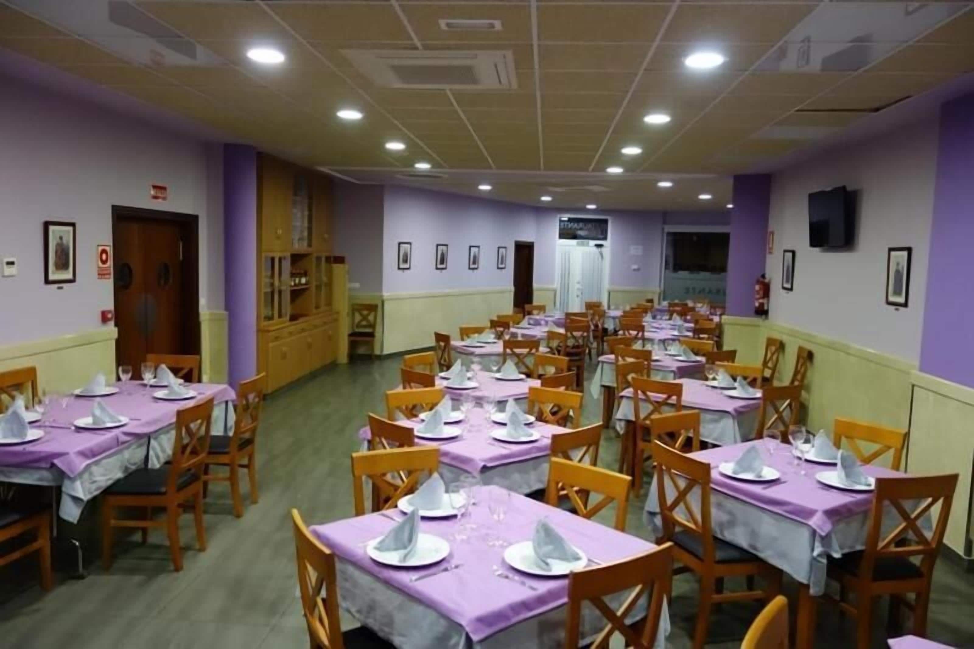 A dining area with multiple tables set for service, featuring purple tablecloths and white plates.