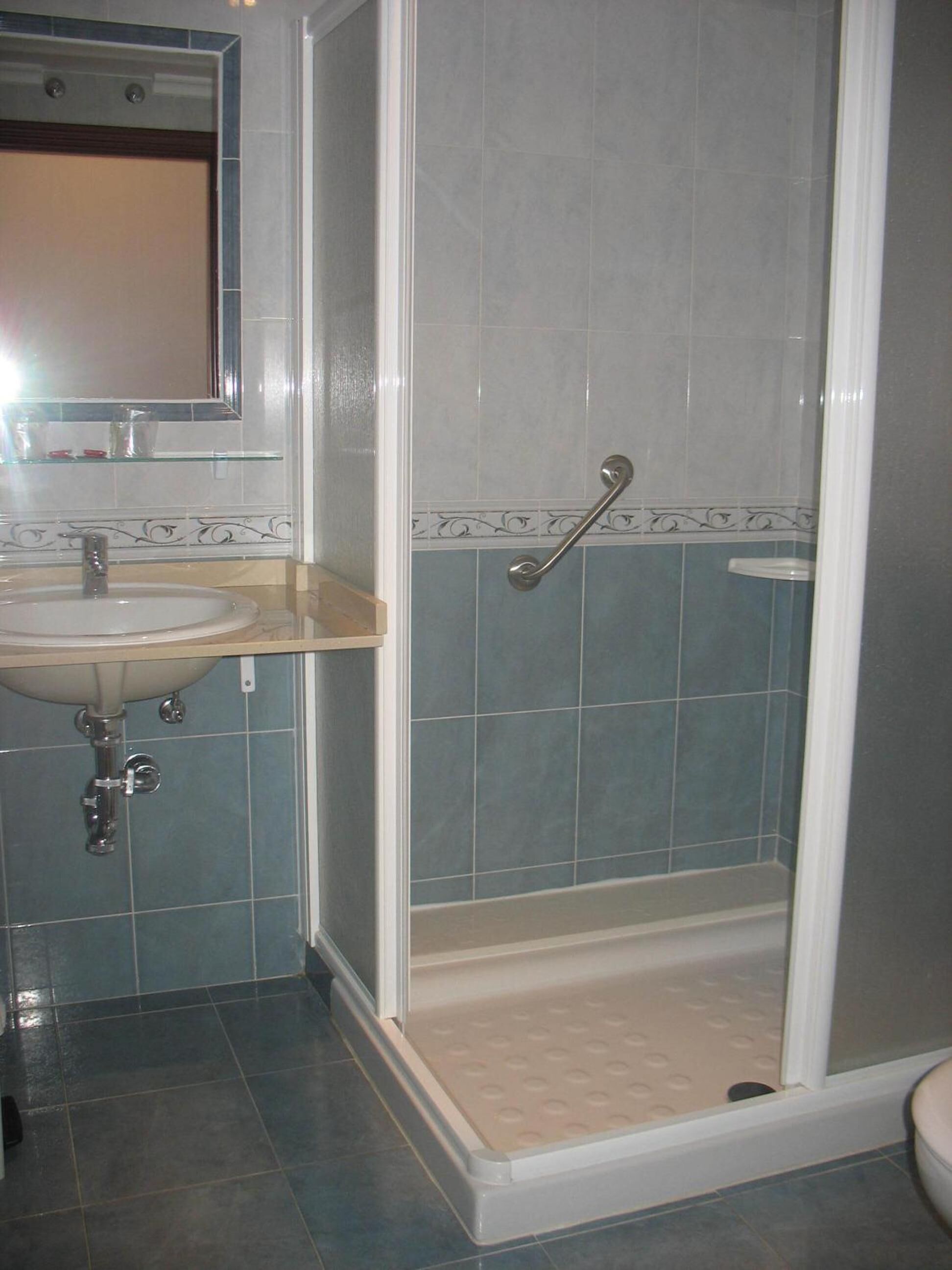 Un baño con lavamanos, espejo y ducha con barra de apoyo.