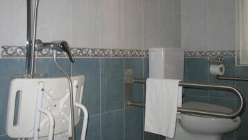 Un baño con ducha, inodoro y barras de apoyo.