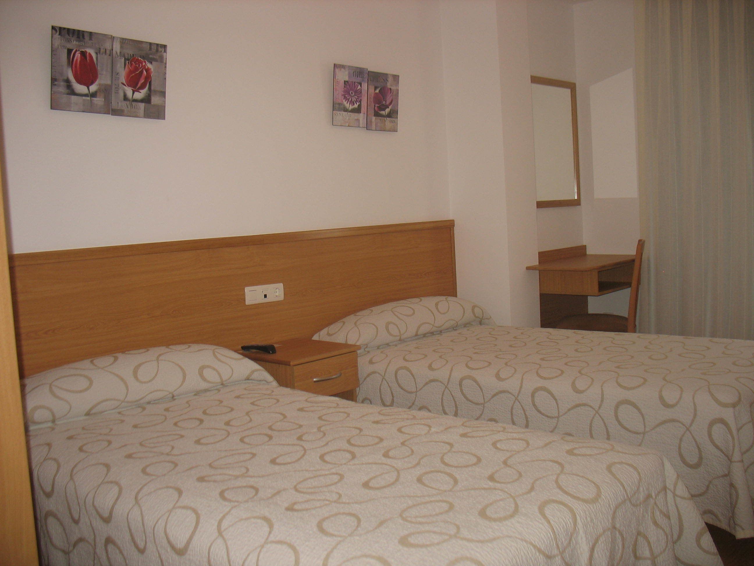 Una habitación de hotel con dos camas, un escritorio y un espejo.