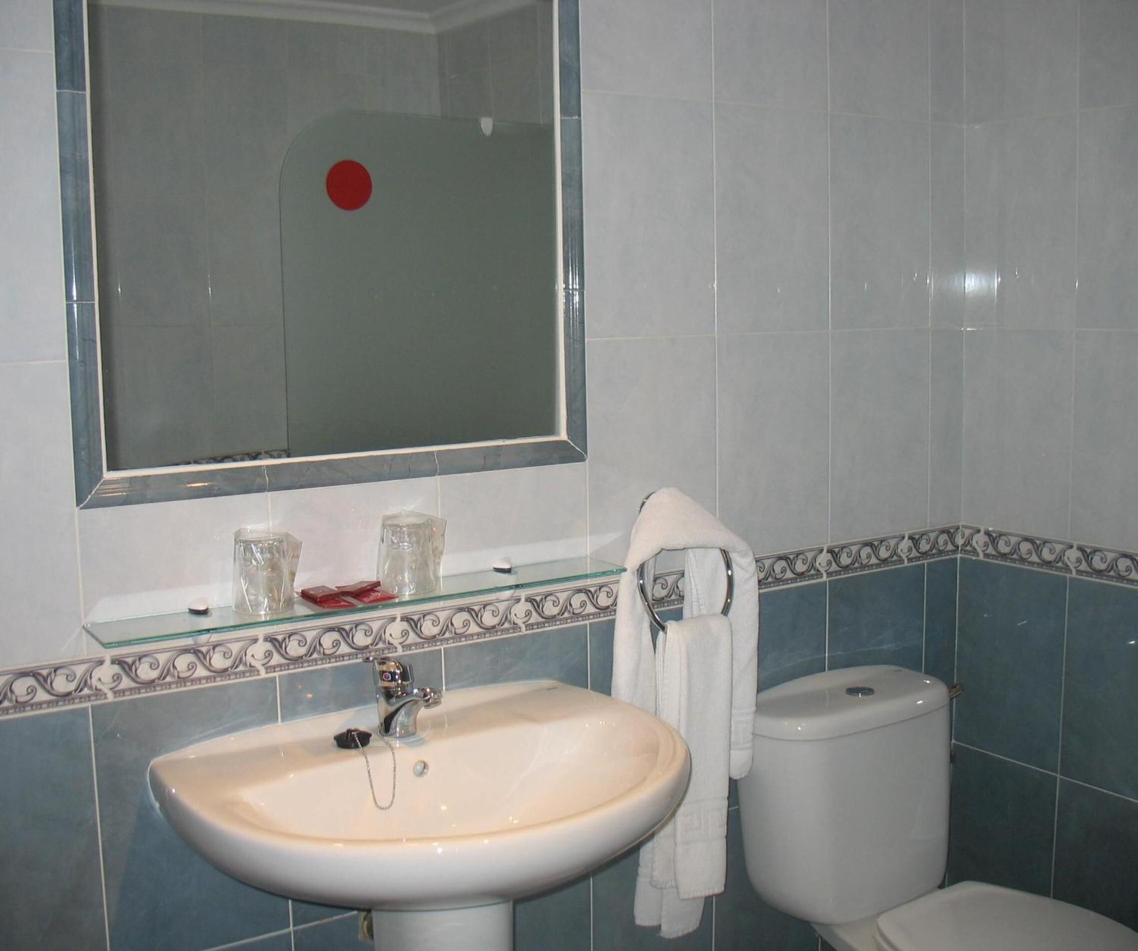 Un baño con lavamanos blanco, espejo y retrete.