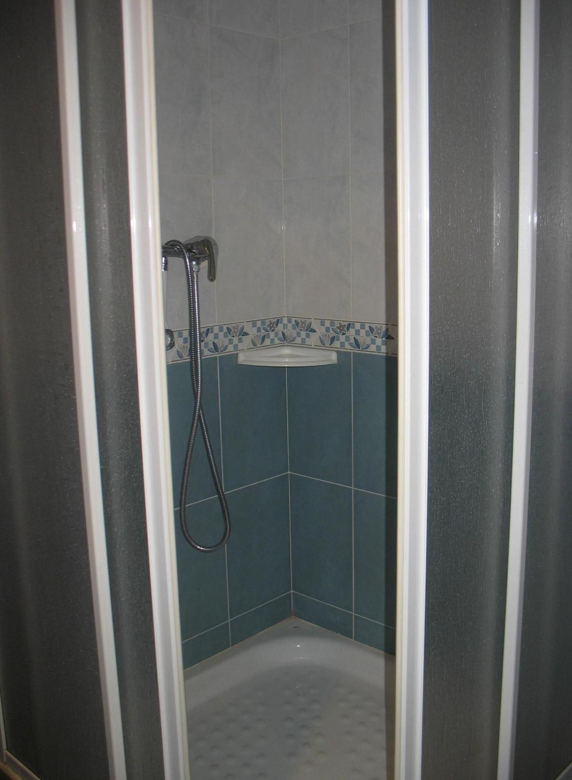 Eine Dusche mit Handbrause, ein Eckwaschbecken und blaue sowie weiße Fliesen.