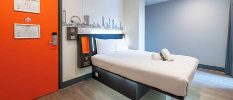 A hotel room with a bed, an orange door, a cityscape wall mural, and a control panel.