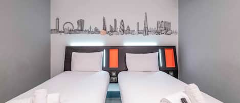 A hotel room with two beds, a city skyline mural, a modern headboard, and a remote control on the bed.