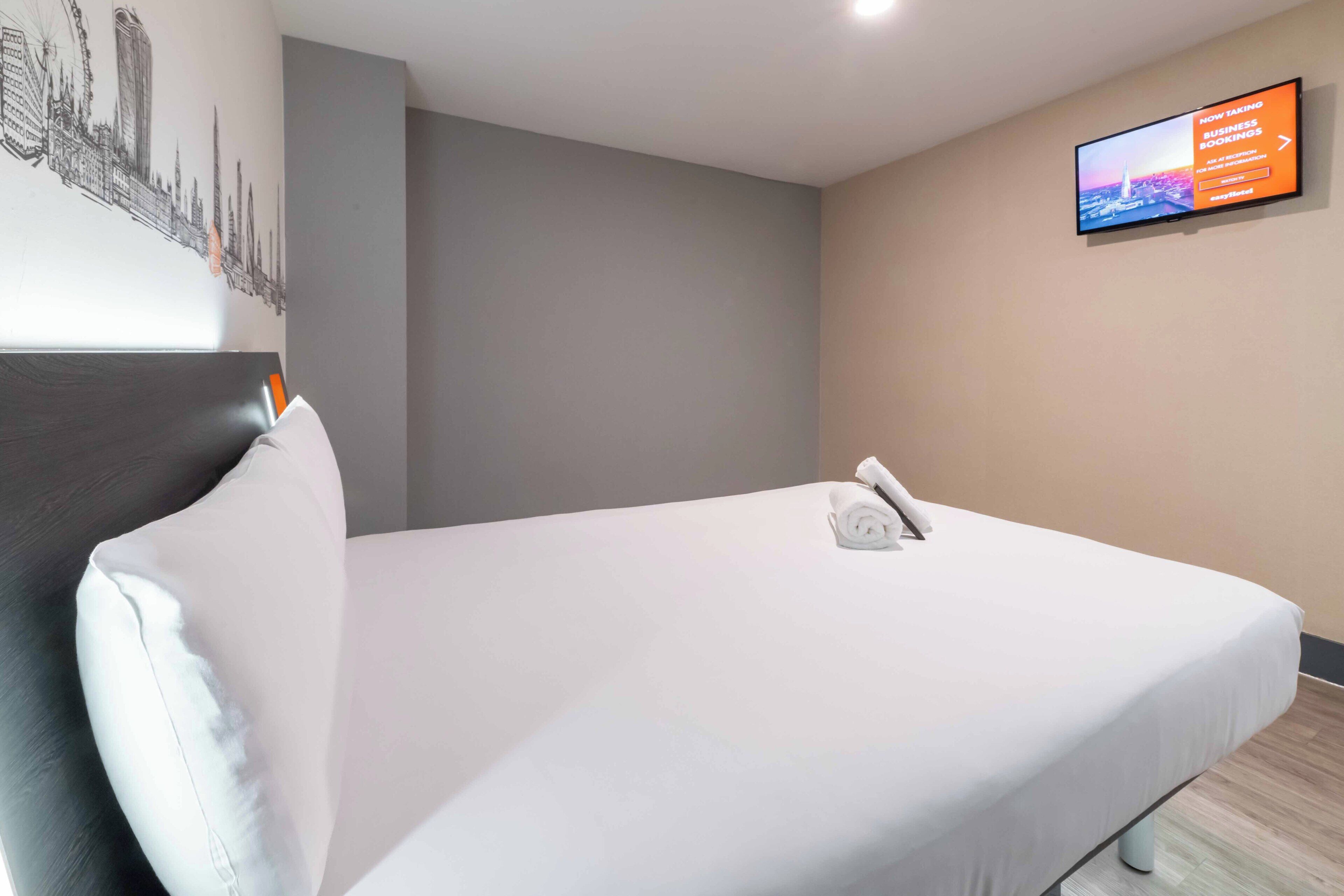 A hotel room with a bed, a television mounted on the wall, and a cityscape mural on the wall.
