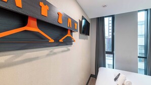 Una habitación de hotel con cama, televisión montada en la pared y ventana con cortinas.