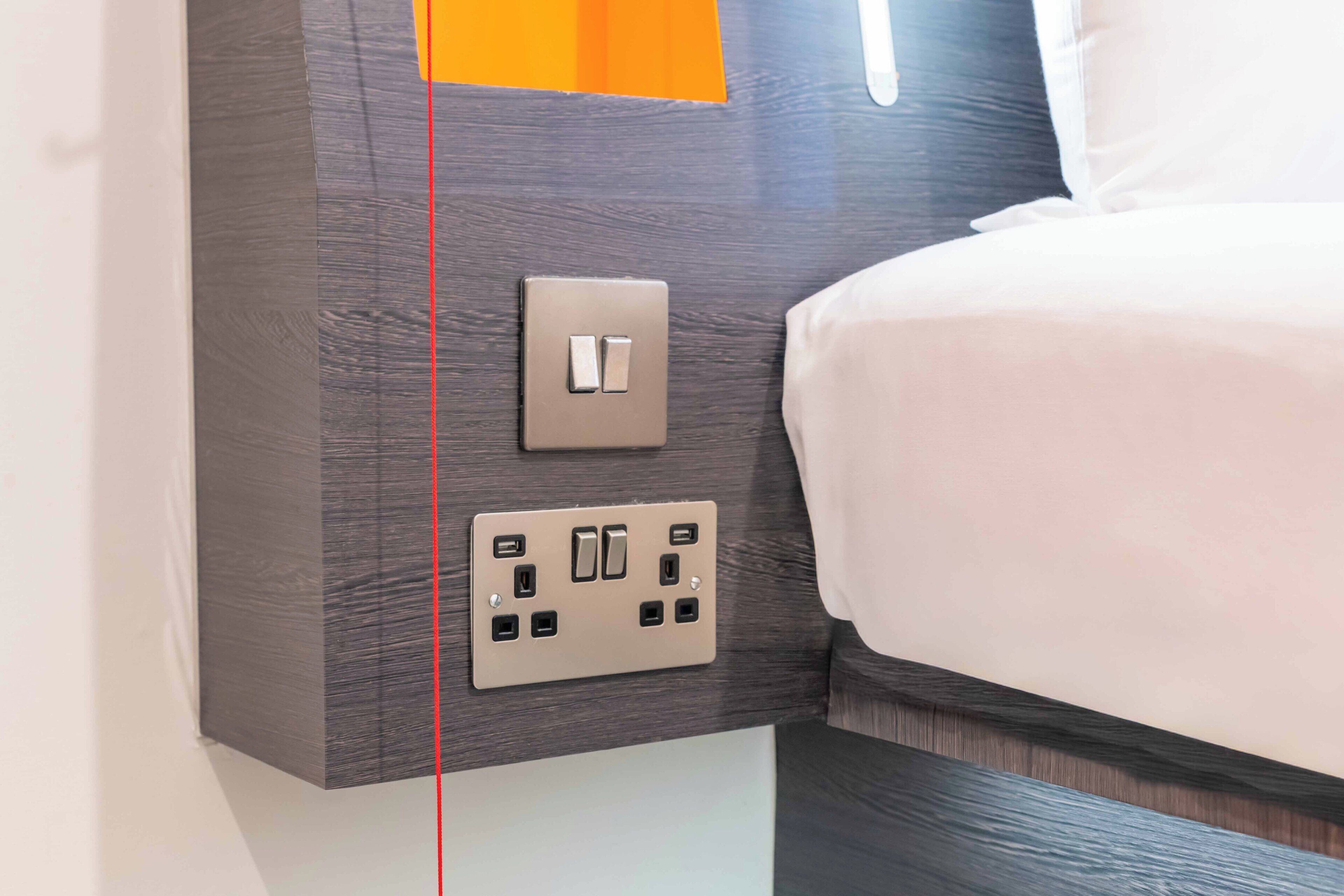 A wall-mounted light switch and electrical outlet in a hotel room.