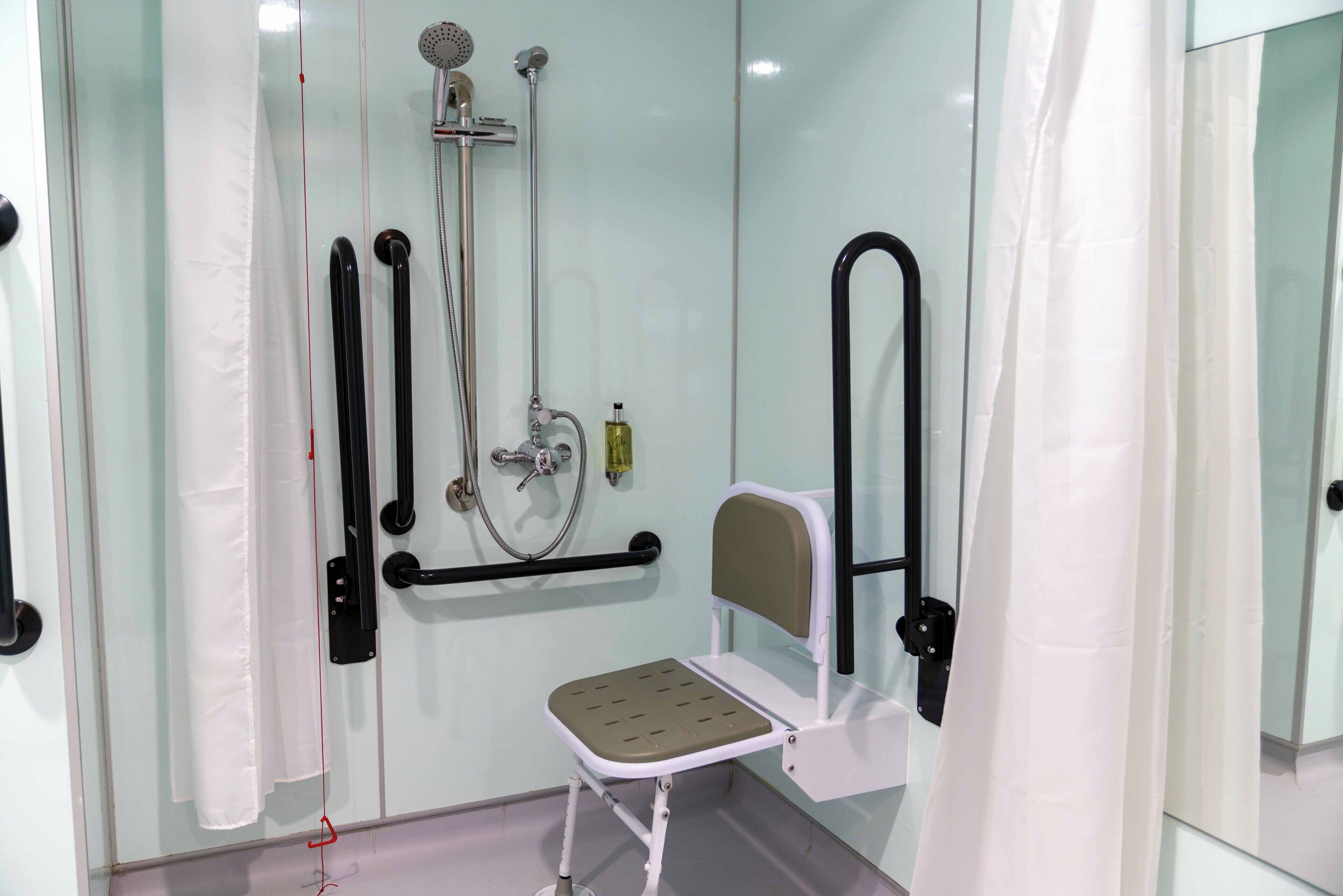 A bathroom with a shower, a toilet, a bidet, and a small stool.