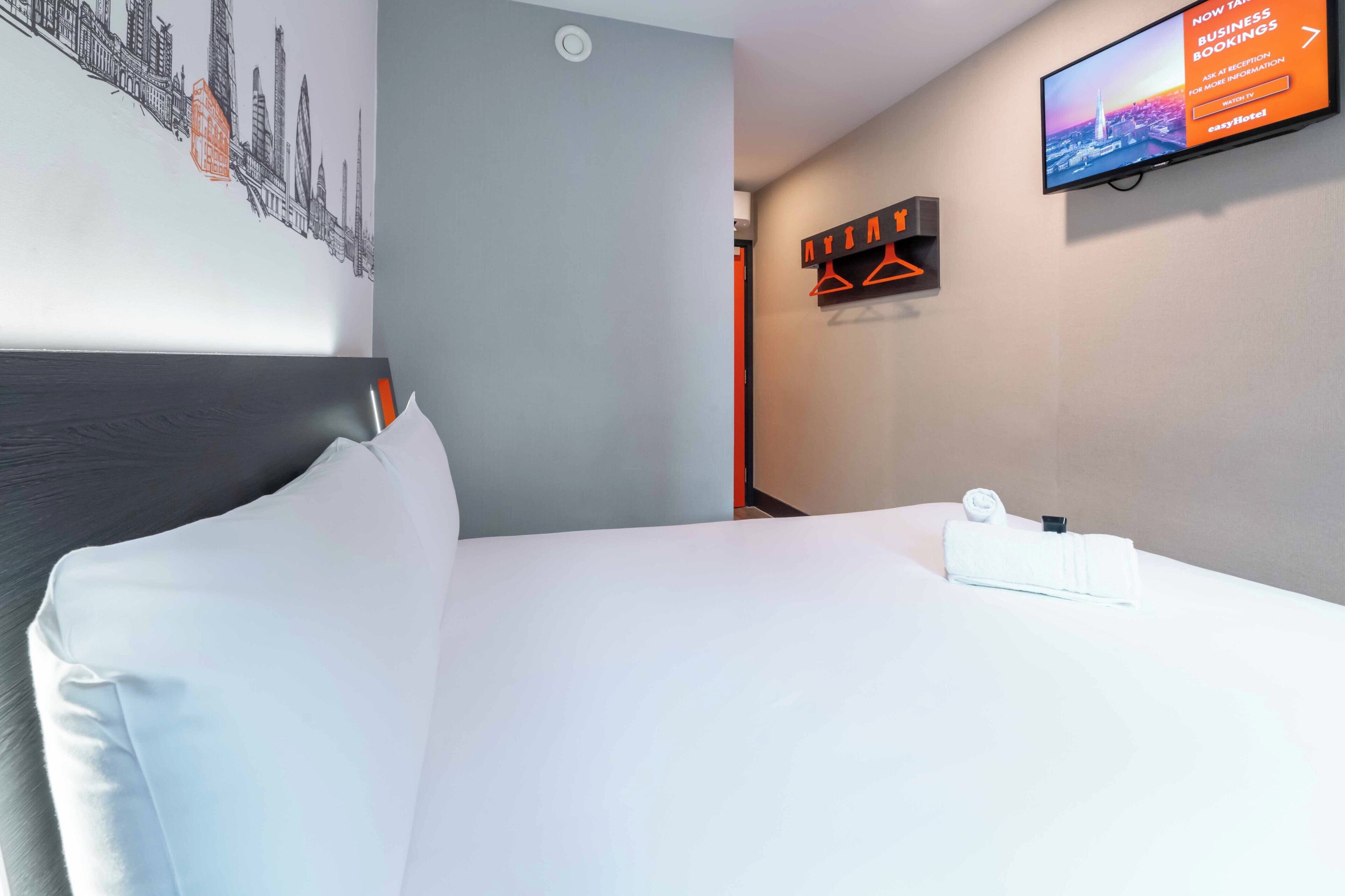 A hotel room with a bed, a television mounted on the wall, and a cityscape artwork on the wall.