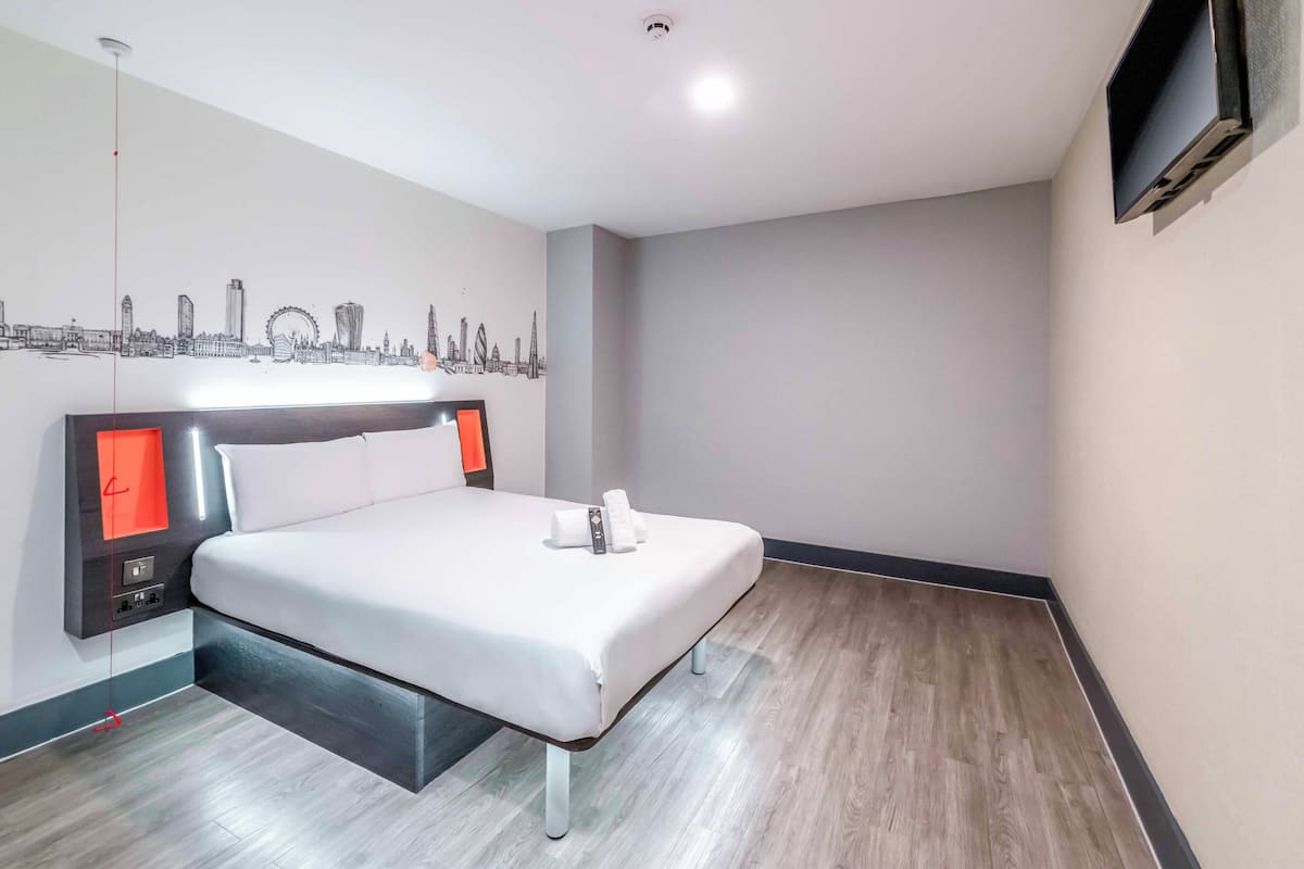 A hotel room with a bed, a cityscape mural, a flat-screen TV, and a wooden floor.