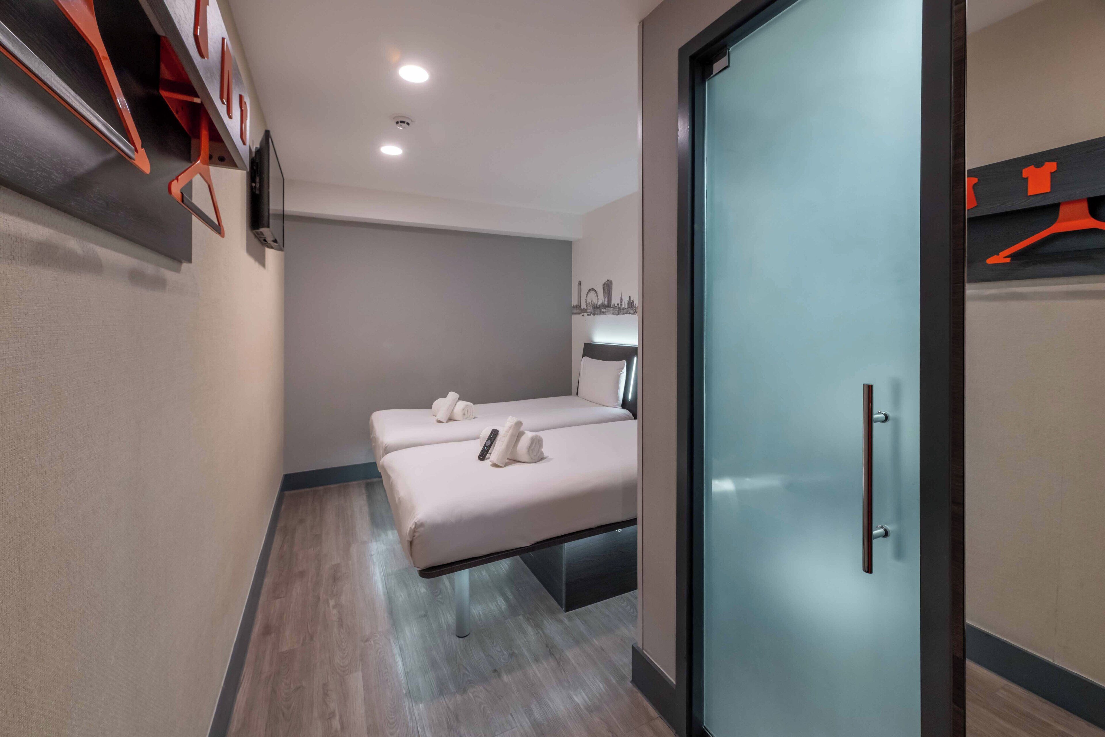 A hotel room with two beds, a glass door, and a wall-mounted TV.