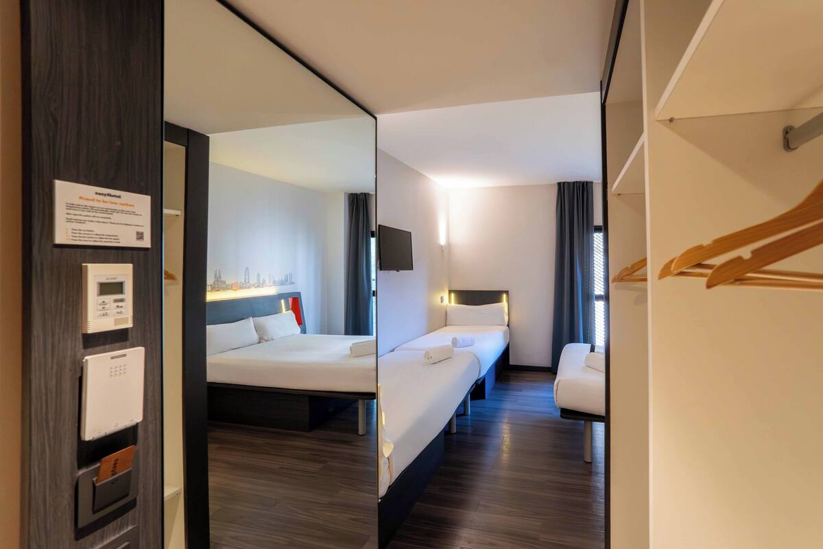 Una habitación de hotel con cama, mesita de noche y un espejo que refleja el cuarto.
