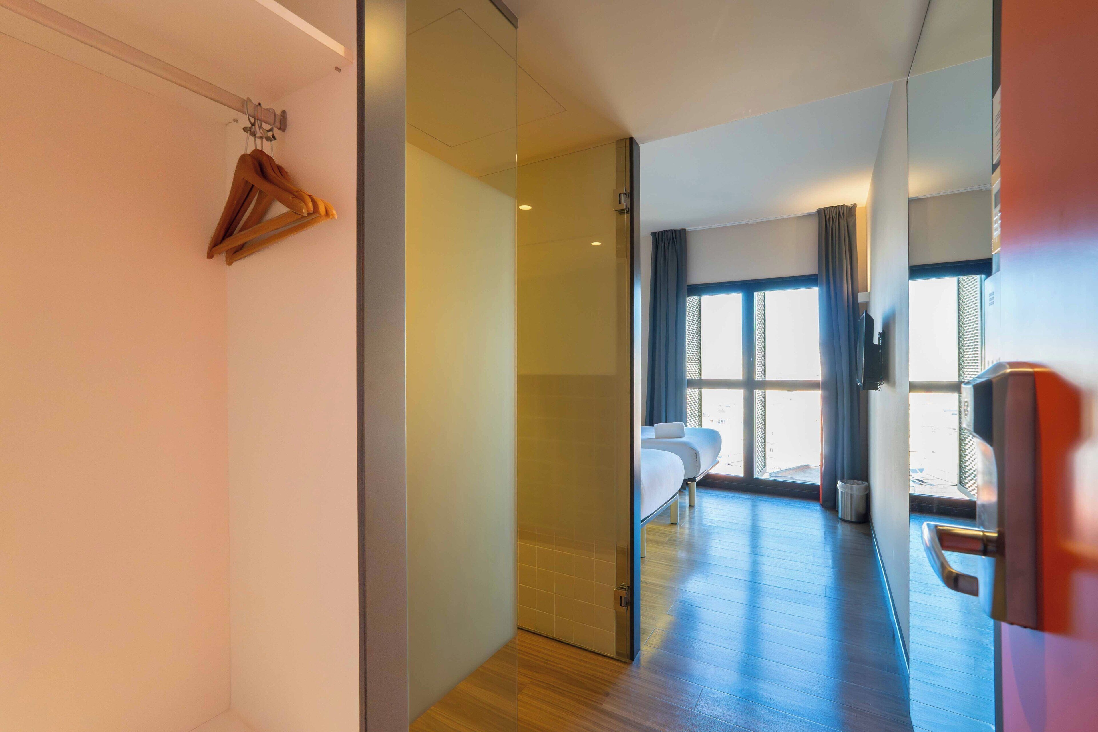 A hotel room with a bed, a seating area, and a view through a large window.