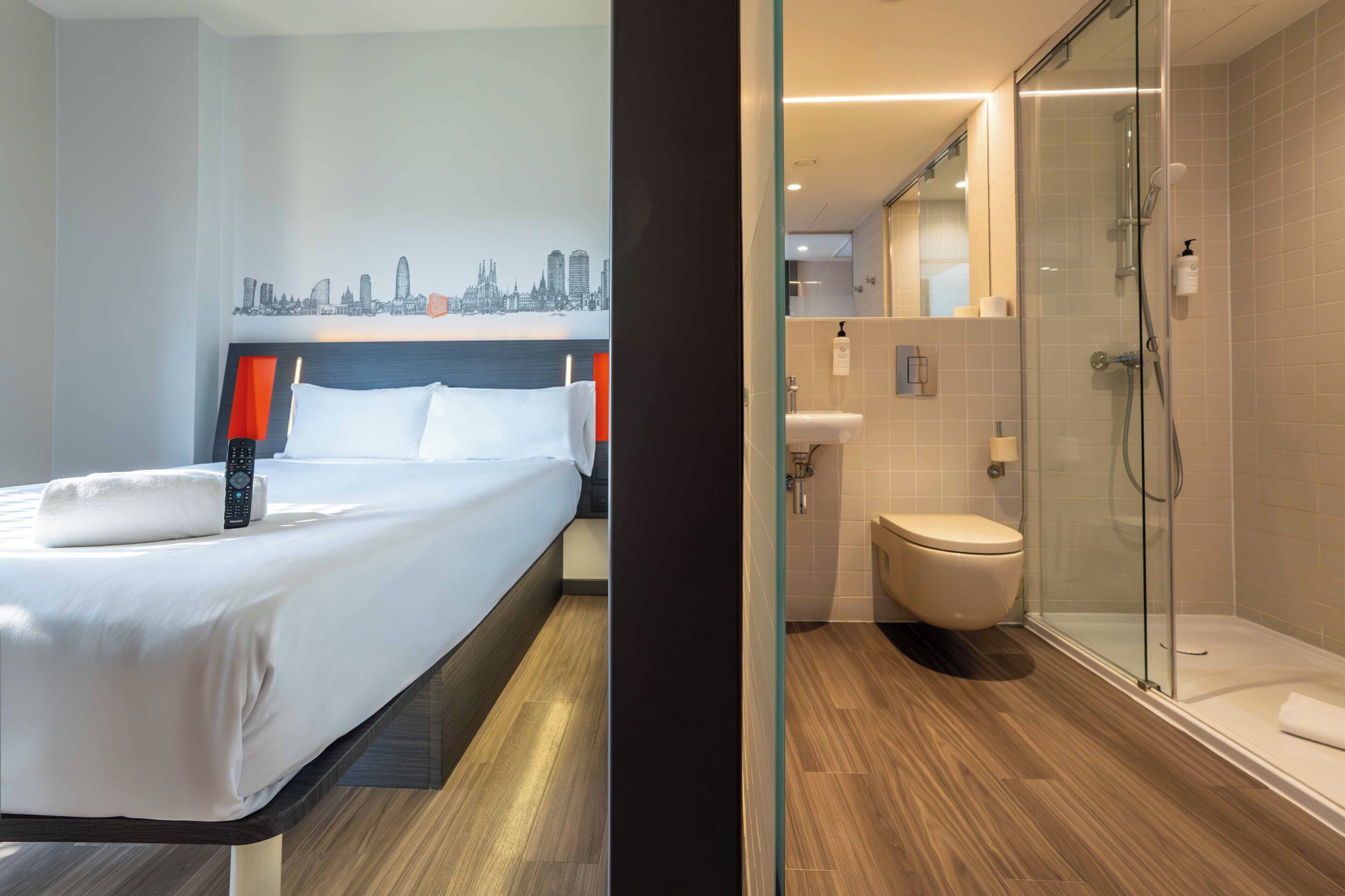 Une chambre d’hôtel avec un lit, un mur décoré d’une vue sur la ville, une douche et des toilettes.