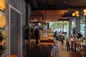 A cafe with wooden tables and stools, a display case with pastries, and a bar area.