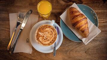 A breakfast setting with a croissant, a cup of coffee, and a glass of orange juice on a wooden table.