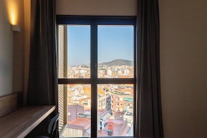 A window with a view of a cityscape, a wooden bench, and a wall-mounted light fixture.