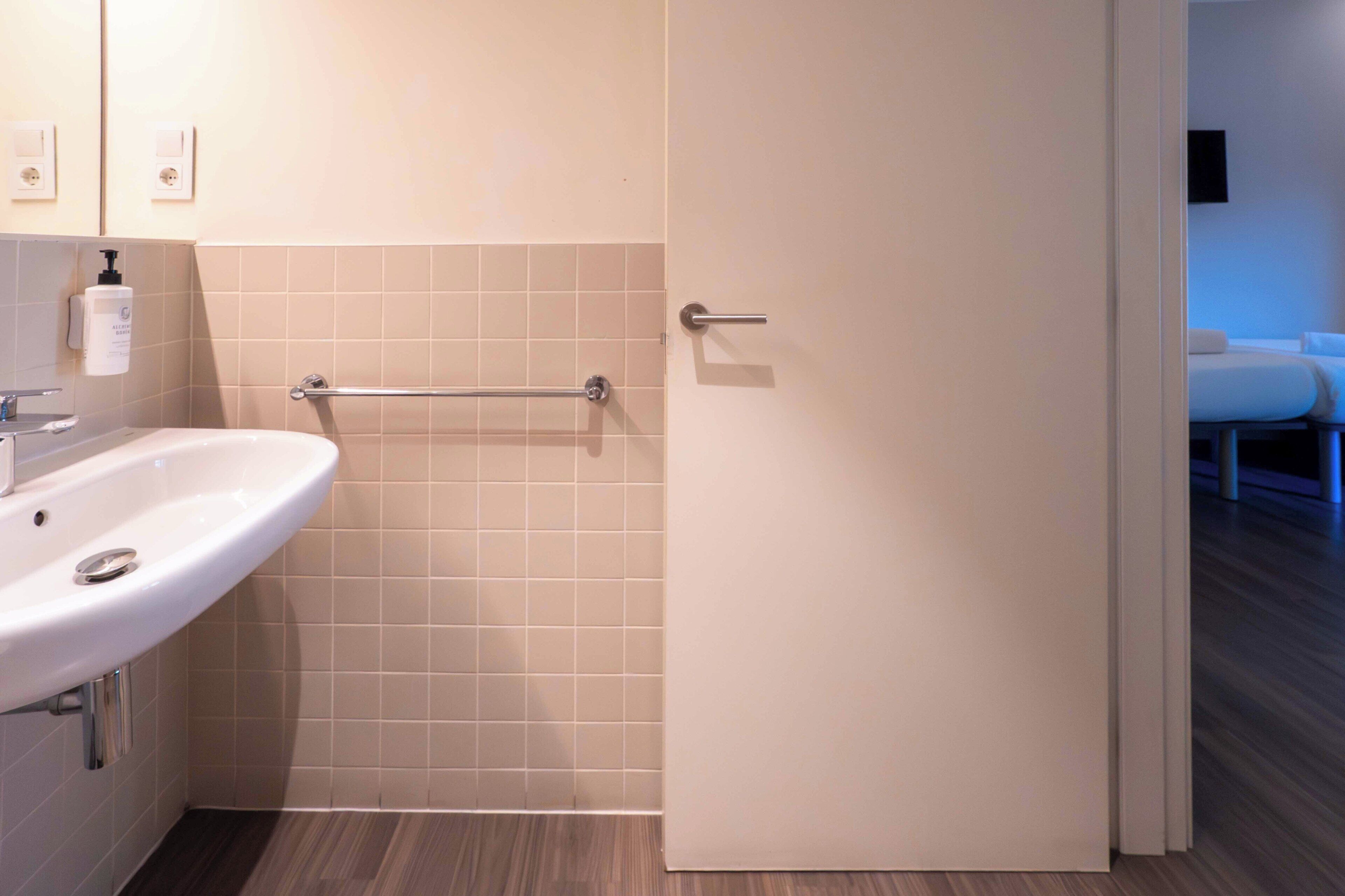 Un baño con un lavabo blanco, un perchero y una puerta que da a un dormitorio.